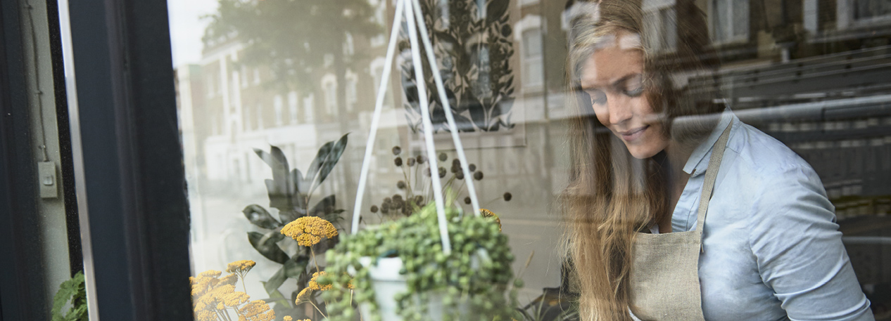 Woman in an apron working in a storefront window with hanging plants