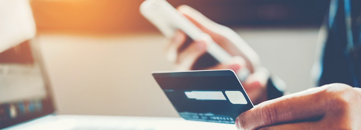 Hand holding a credit card in front of a laptop computer