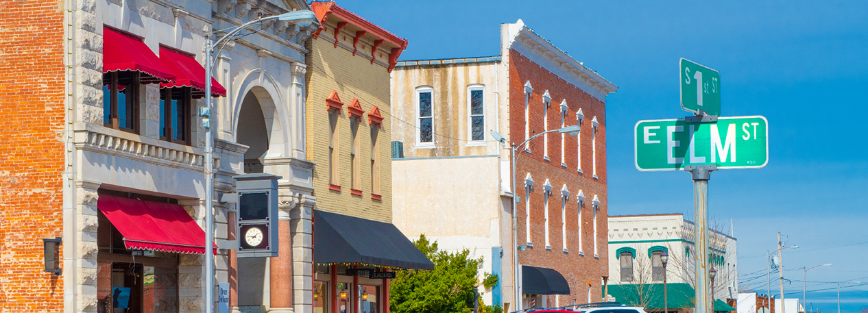 Storefront buildings with a street sign for 1st and Elm in the foreground