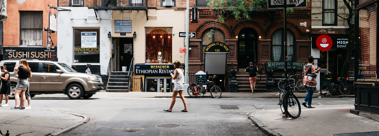 City street corner with pedestrians walking in front of restaurants and shops