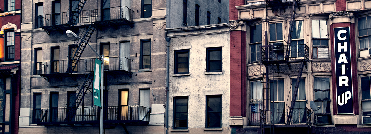 Row of urban buildings, including a residential building with a metal fire escape and a store with vertical sign that reads "Chair Up"