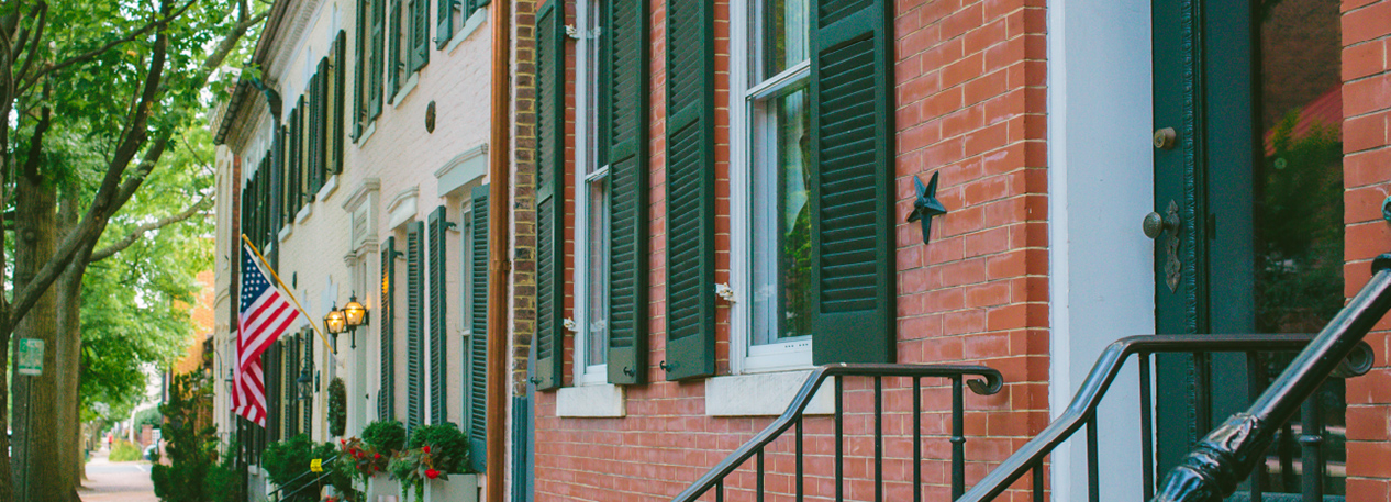 Row of brick townhouses with green shutters, one of which is displaying an American flag