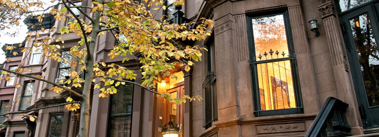 Row of brownstone townhouses at dusk, with windows lit from the inside