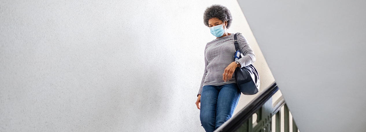 Woman descends staircase while wearing a mask.