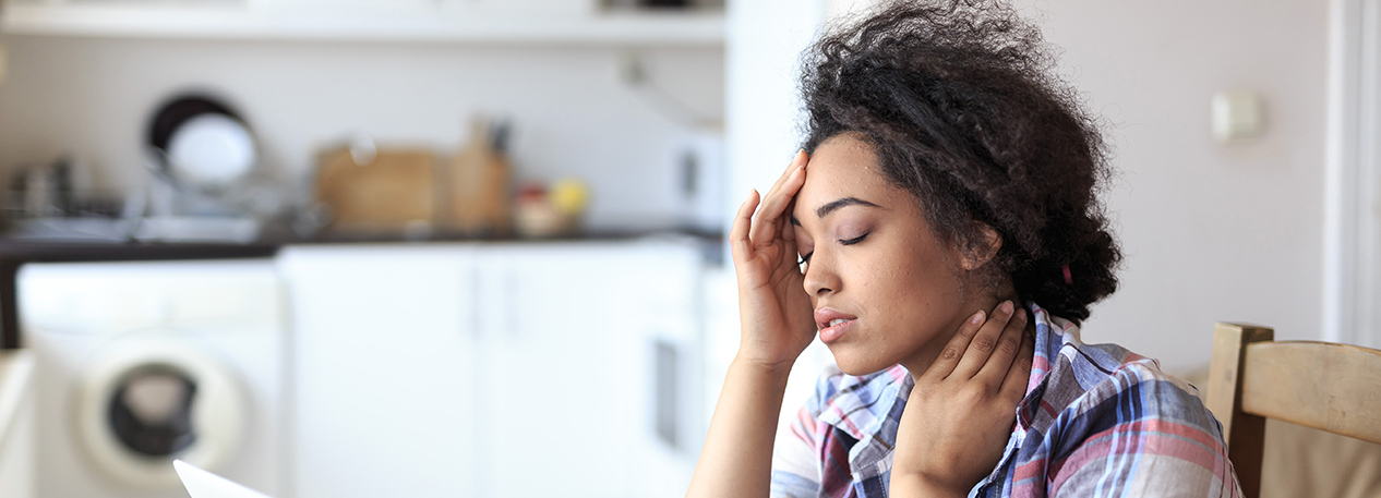 Woman with pained look touching her forehead, looking at a laptop.