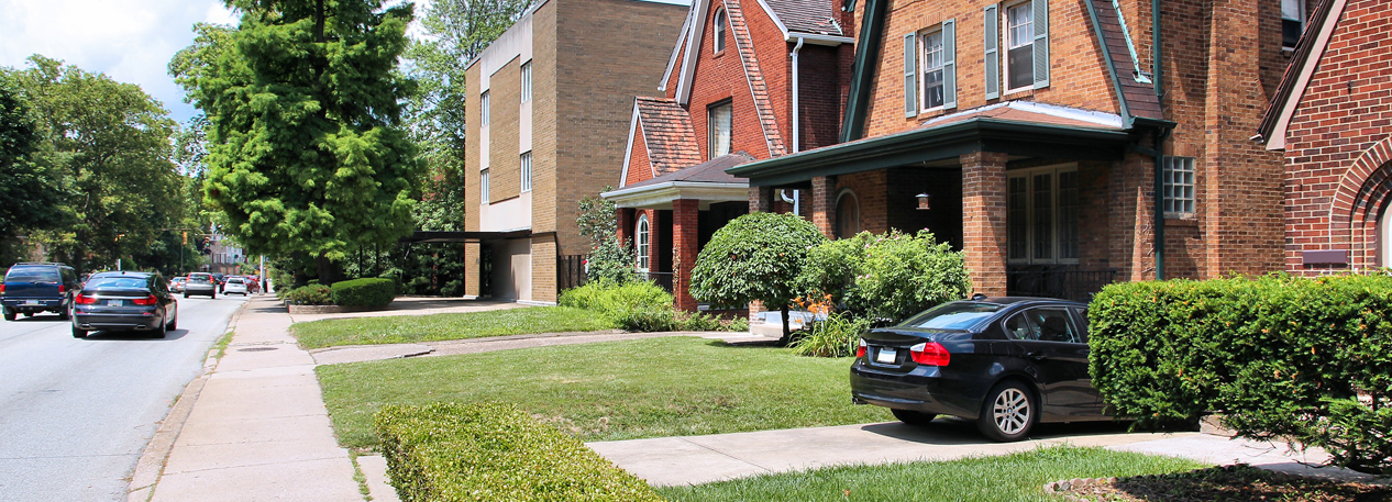 Residential brick homes on a tree-lined street with cars in the driveways.