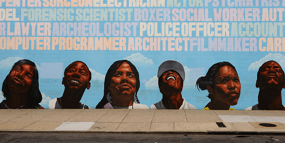 Mural on a wall depicting the heads of six people looking up at the names of various careers.
