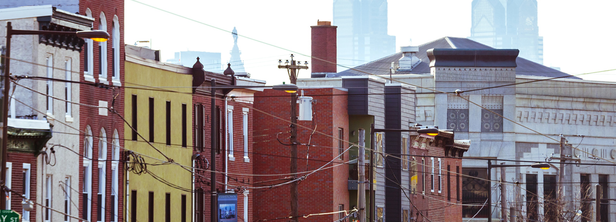 Row of city buildings with the skyline of Philadelphia in the distance.