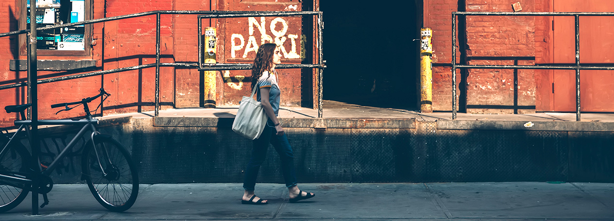 Woman walking down the street with tote bag, passing in front of a warehouse loading dock