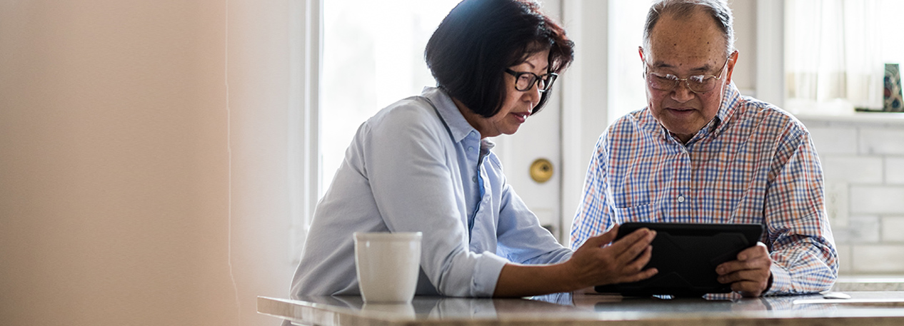 An older couple look at a tablet together at the breakfast table.