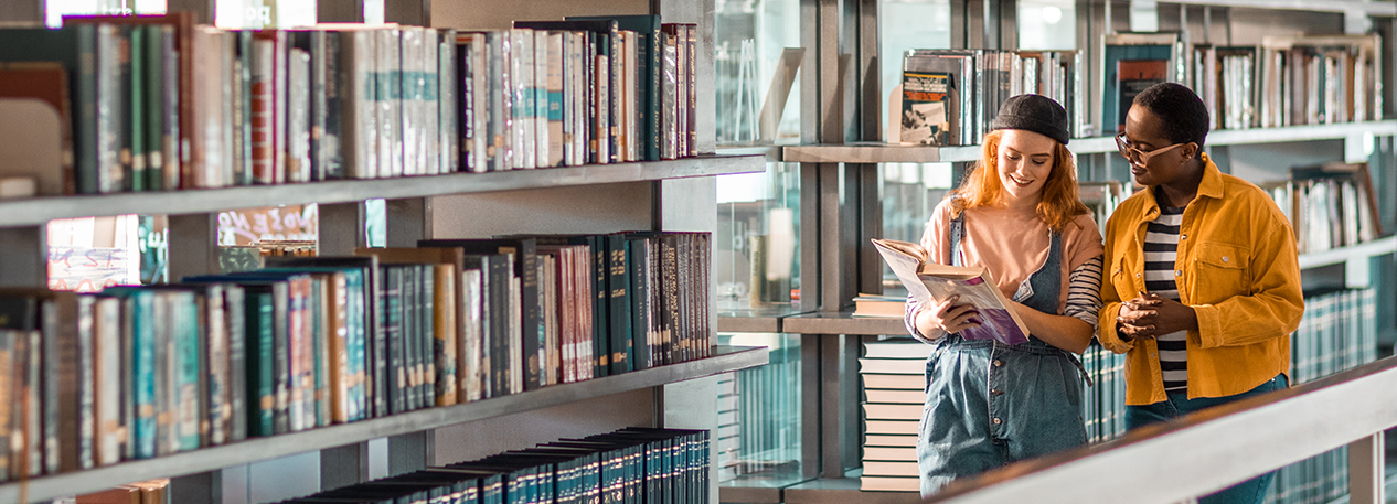 Two students are engaged in conversation as they walk through a library. 