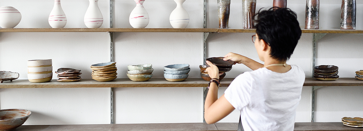 Woman placing vases and bowls on a display shelf in a pottery store