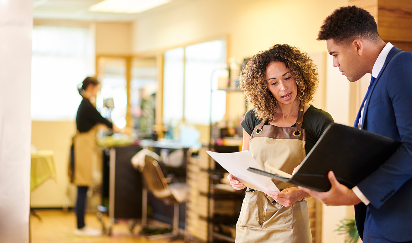 Salon owner speaking with a man in a suit holding an open document portfolio.