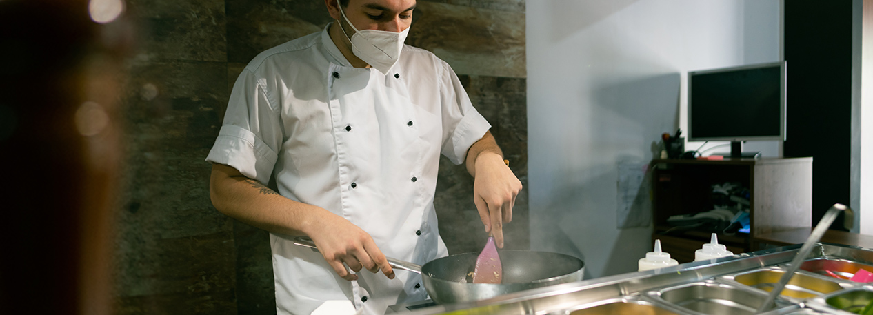 Restaurant worker in a white chef's coat cooking in a kitchen.
