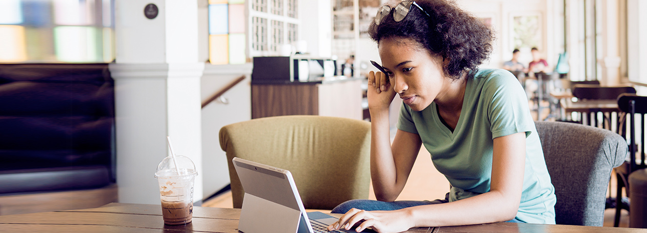 A college student works on her tablet with an iced coffee close by.