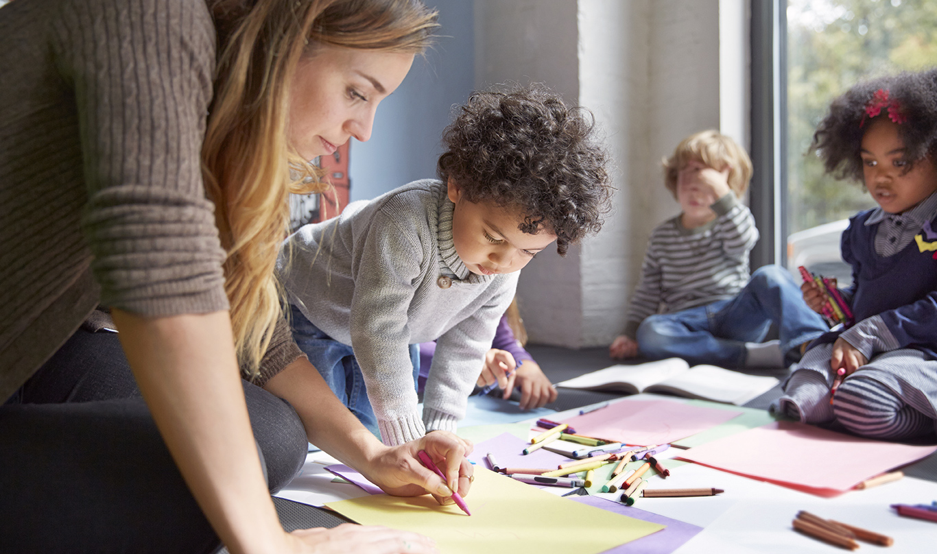 Young children look on as a teacher provides instruction at a day care program.
