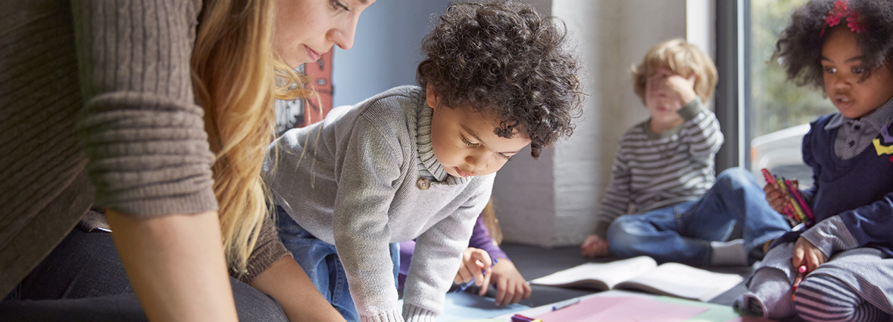 Young children look on as a teacher provides instruction at a day care program.