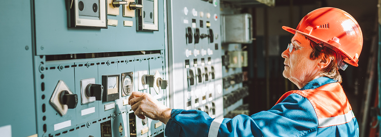 A factor worker, wearing a hard hat and uniform, adjusts the settings on a machine.