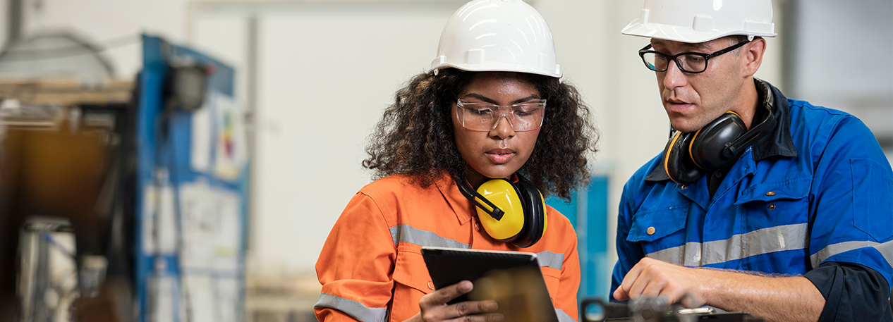 Workers in a factory wearing hardhats and looking at a tablet computer.