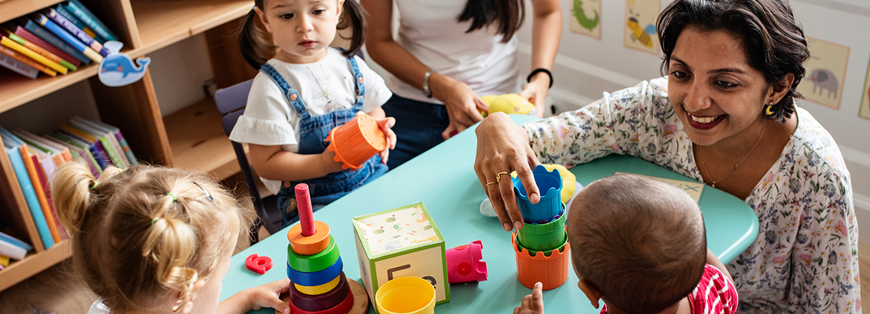 Young children at a daycare center play with toys and interact with their teacher.