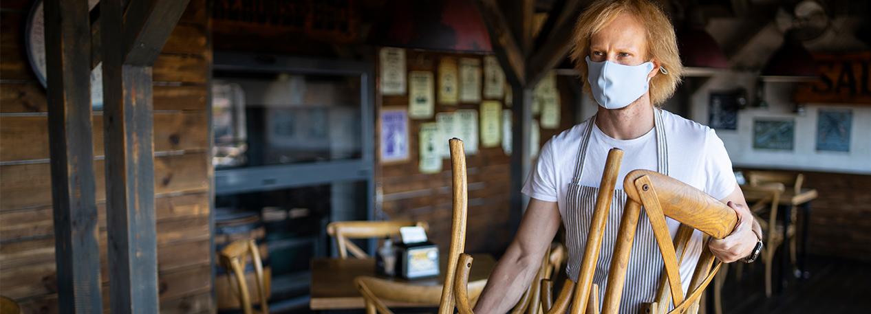Restaurant worker wearing a mask and placing a chair upside-down on a table.