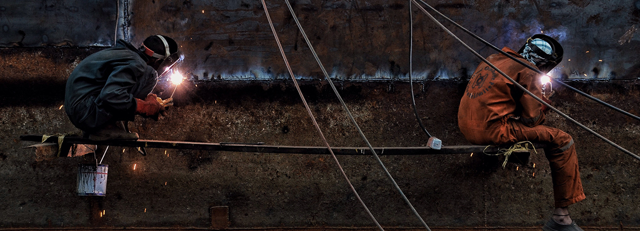 Two workers in masks, sitting on platform, welding