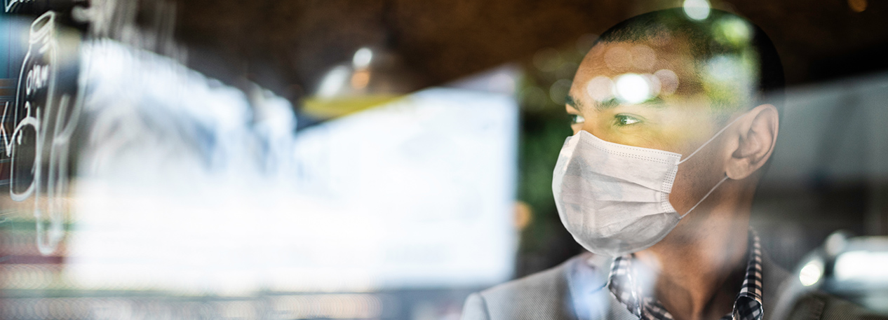 A small business owner wears a face mask and looks out the window of his storefront.