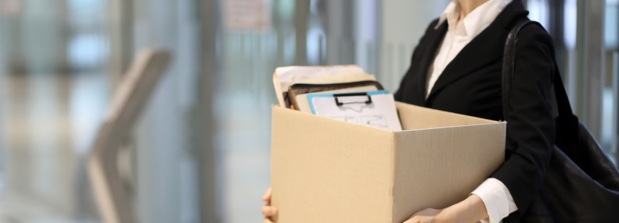 A woman is leaving her office job with a cardboard box of paperwork.