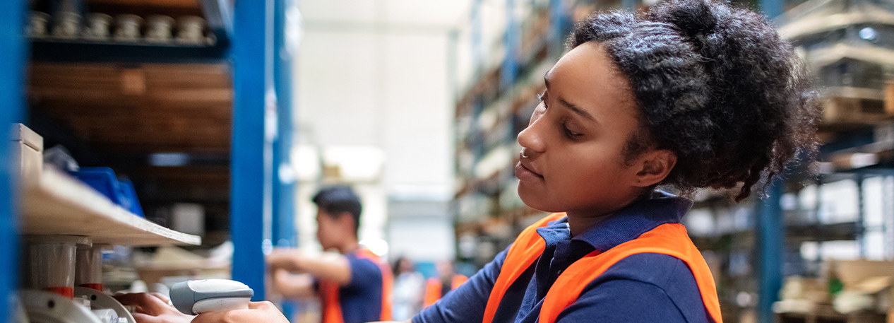 Female warehouse worker in safety vest scanning items on shelf.