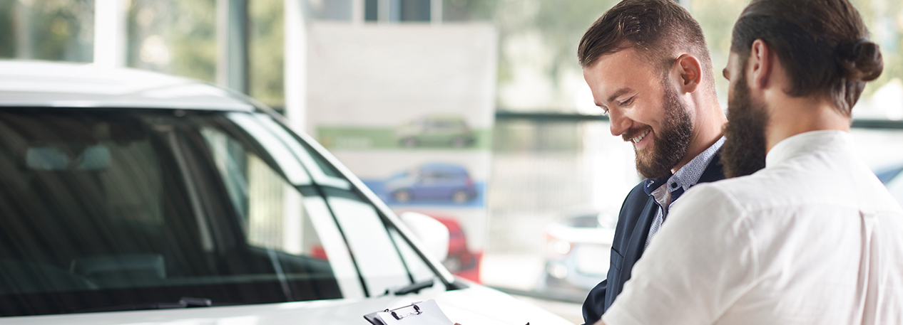 Man signing a document on a clipboard at a car dealership