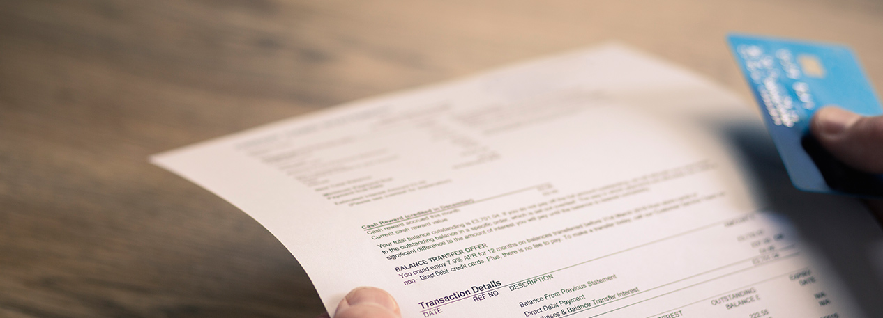 A close-up image of hands holding a billing statement and a credit card.