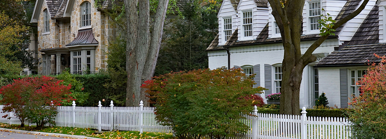 Upscale houses behind a picket fence on a tree-lined street