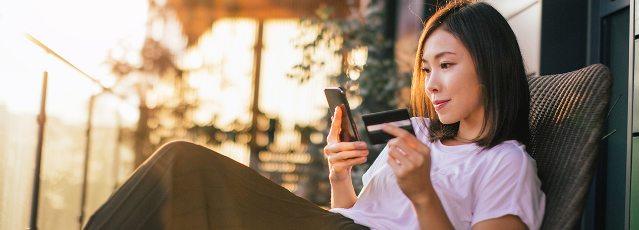 A woman sits on her porch with her phone in one hand and her credit card in the other hand.