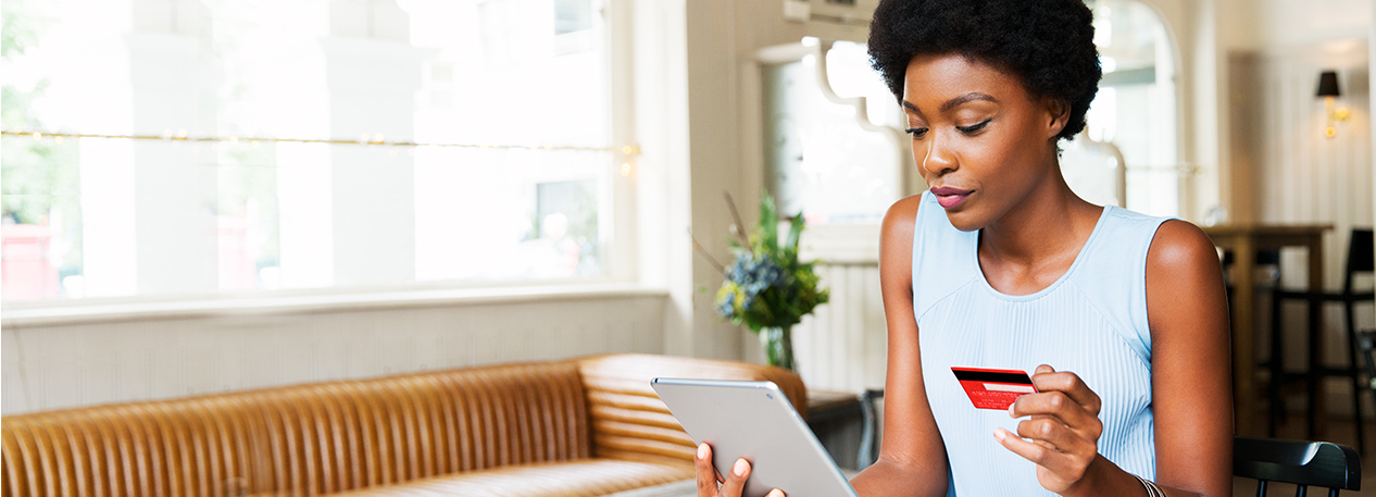 Woman holds a credit card in one hand and a tablet in the other.