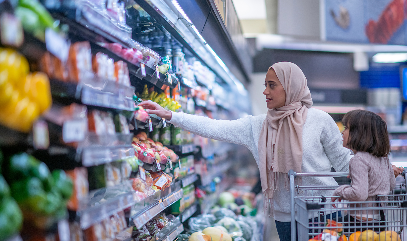 Woman wearing a hijab in a grocery store with a child sitting in a shopping cart.