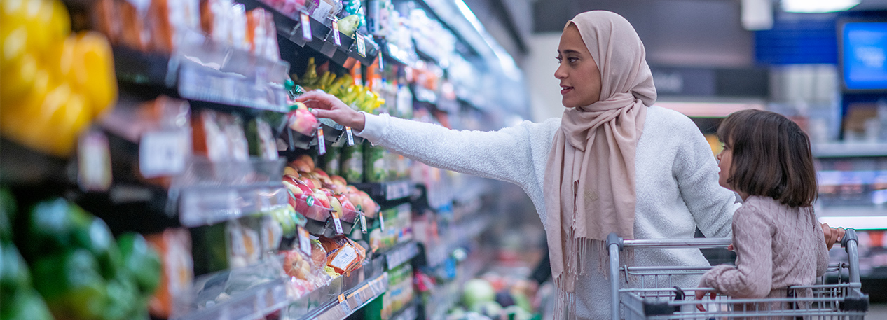 Woman wearing a hijab in a grocery store with a child sitting in a shopping cart.