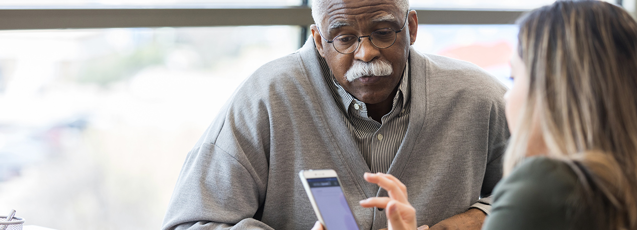 Older man talking to a younger woman holding and browsing on a cell phone
