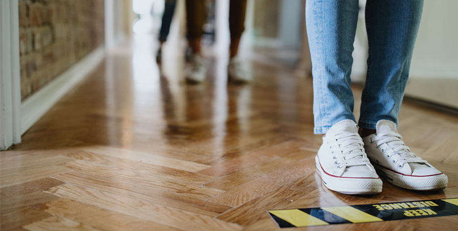 The feet of people standing in line, behind social distancing markers on the floor.