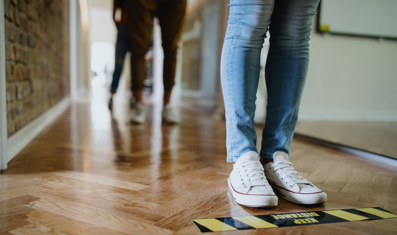 The feet of people standing in line, behind social distancing markers on the floor.