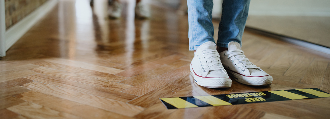 The feet of people standing in line, behind social distancing markers on the floor.