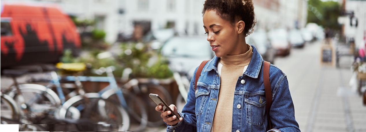 Woman looking at her cell phone, standing next to a bike rack on a city street