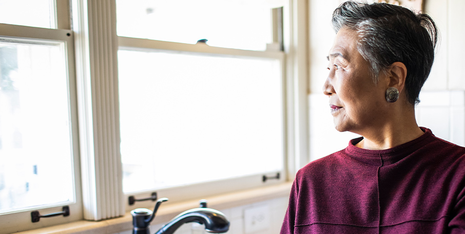 A senior woman looks out her kitchen window.