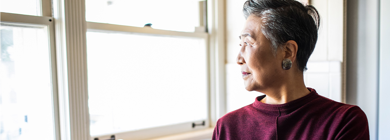 A senior woman looks out her kitchen window.