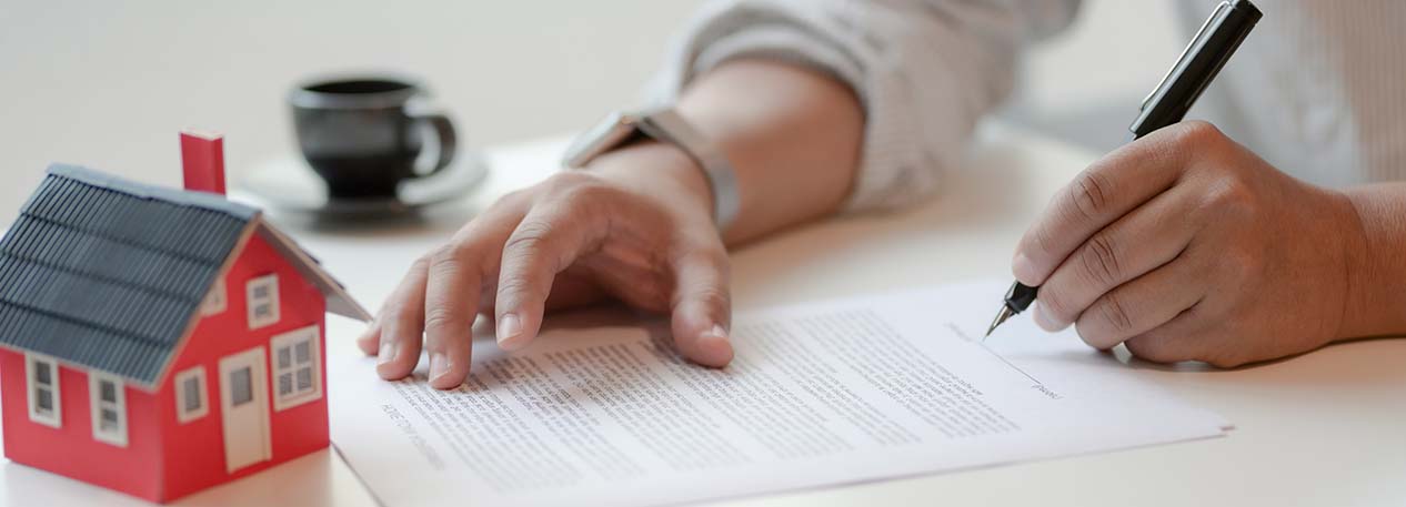 Person signing a contract with a model of a red house on the table.