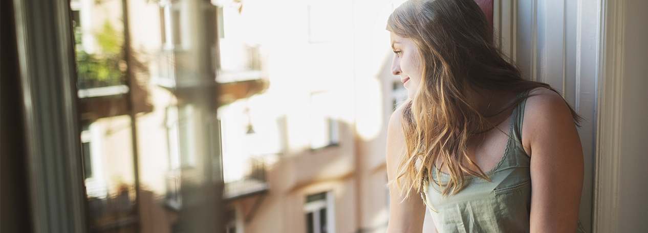 A woman looks down at the street from her apartment window.