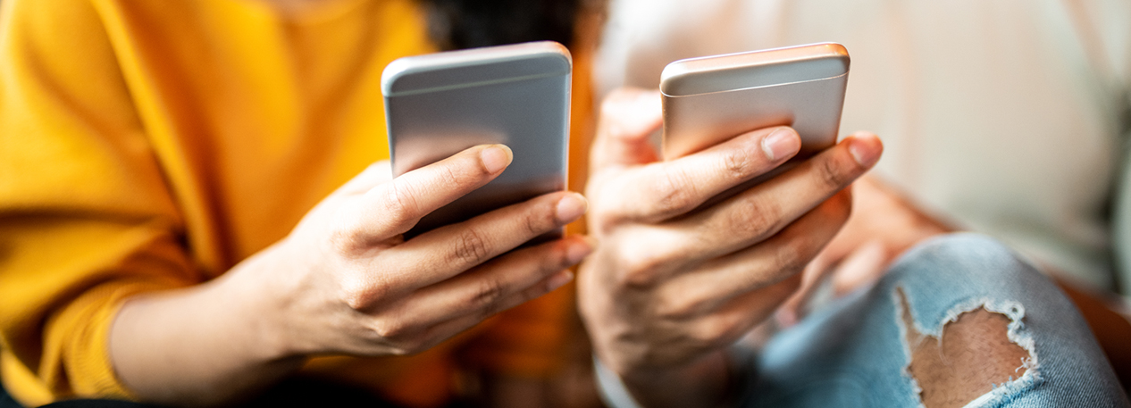 Two people sitting side-by-side and holding their cell phones close together