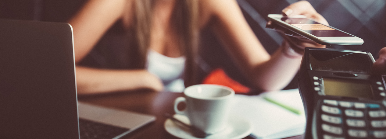 Woman with laptop in a cafe paying on a hand-held reader, using contactless payment on her cell phone