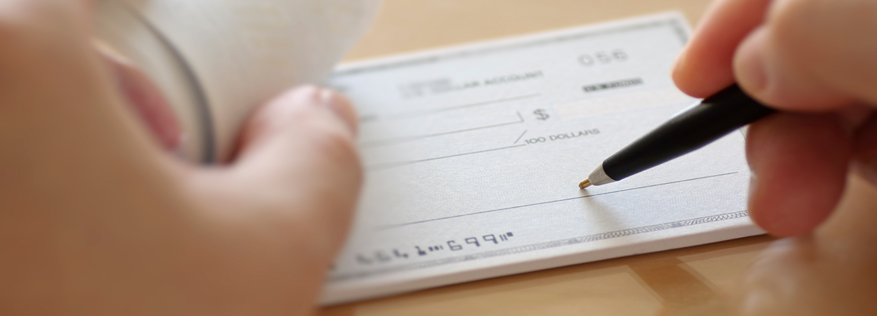 Hands holding a pen and signing a paper check