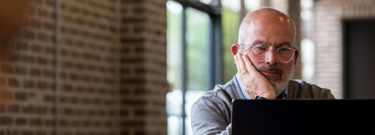 A bald man with glasses reviews bills on his lap top.