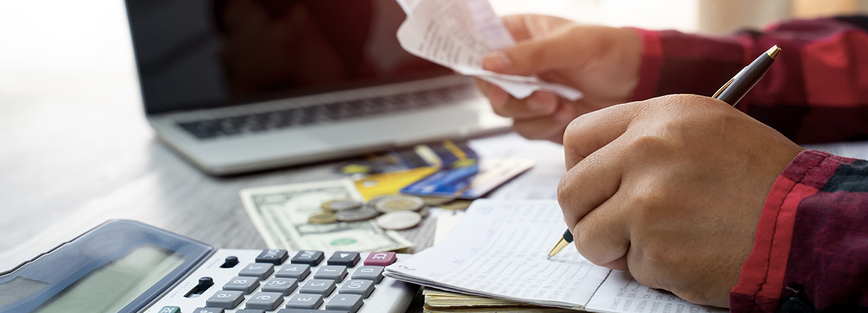 Person at a desk with money, a calculator, and a laptop computer, writing on a form.